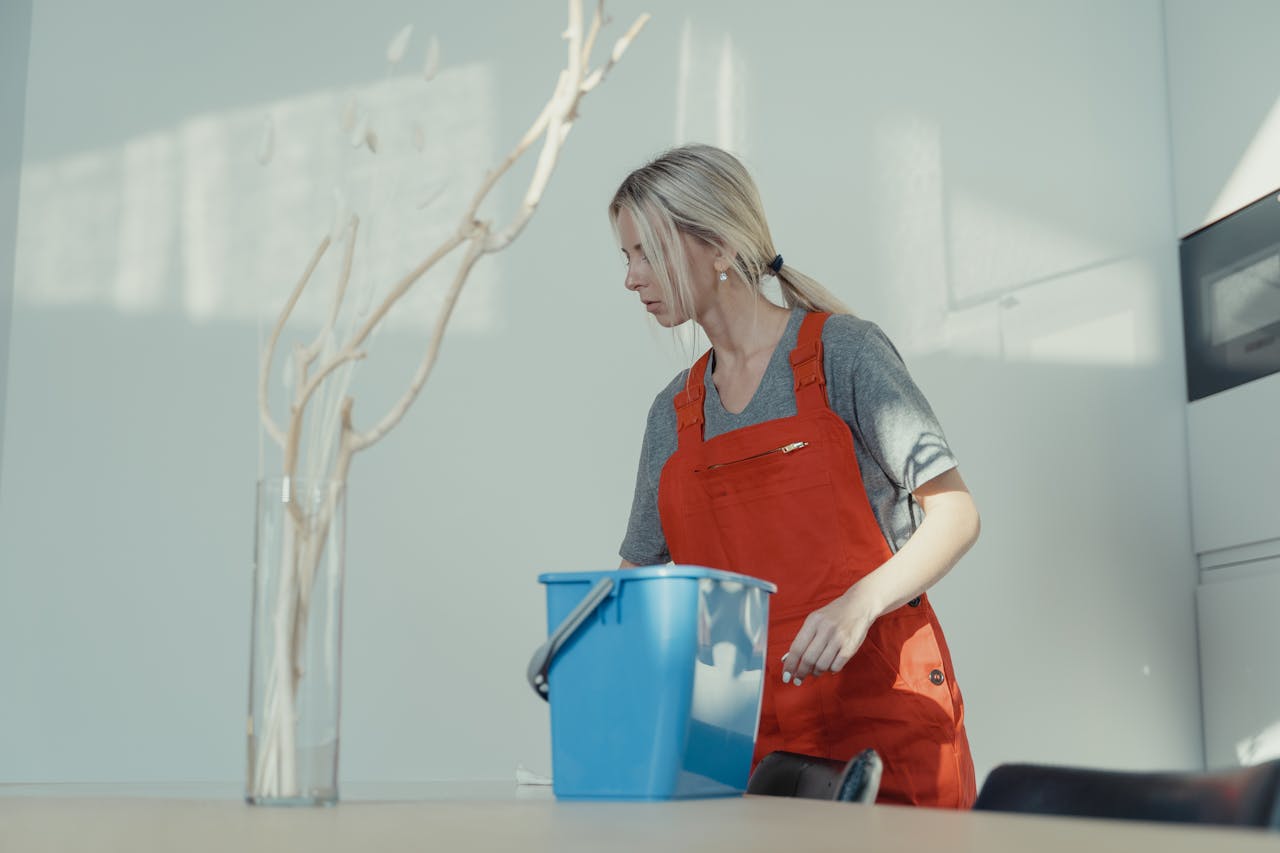 services-01 A woman in a red uniform cleans indoors with a blue bucket, ensuring a spotless environment.